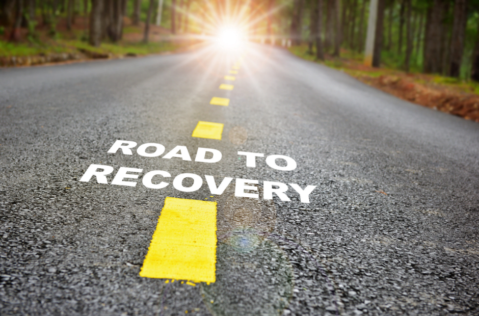 Image of a road leading toward the sun in the distance with the words "Road to Recovery" on the asphalt
